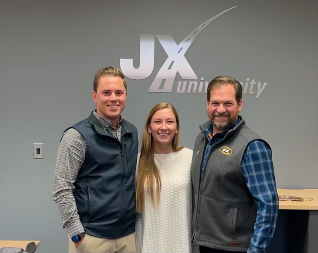 Austin Freeman, Hannah Freeman, and Eric Jorgensen in front of JX Enterprises logo